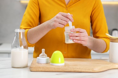 Photo of Mother making baby formula in feeding bottle at table indoors, closeup