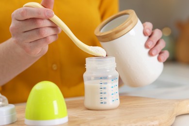 Photo of Mother making baby formula in feeding bottle at table indoors, closeup