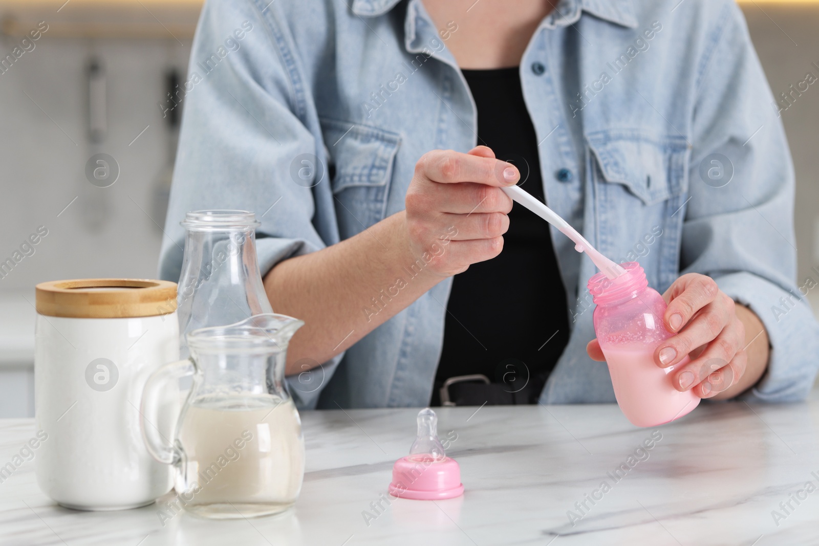 Photo of Mother making baby formula in feeding bottle at table indoors, closeup