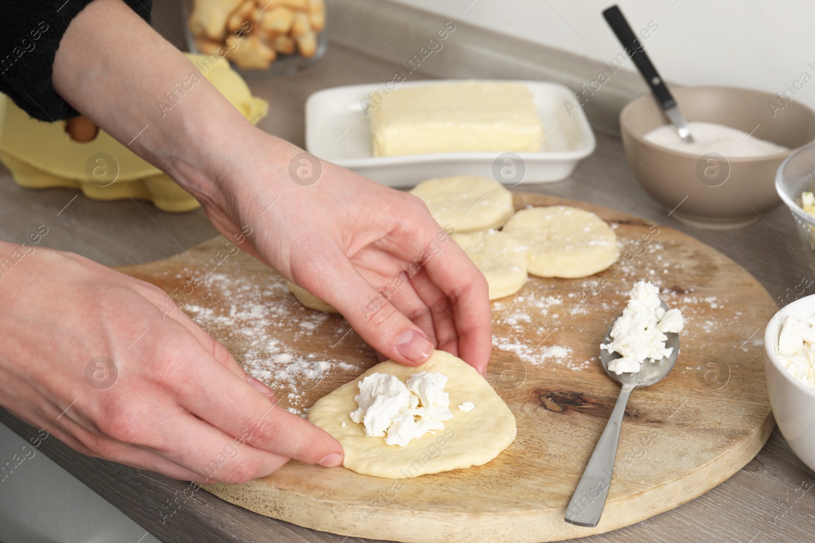 Photo of Woman making pirozhki (stuffed pastry pies) with cottage cheese at countertop indoors, closeup