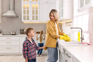 Housewife washing dishes while her kids playing in kitchen