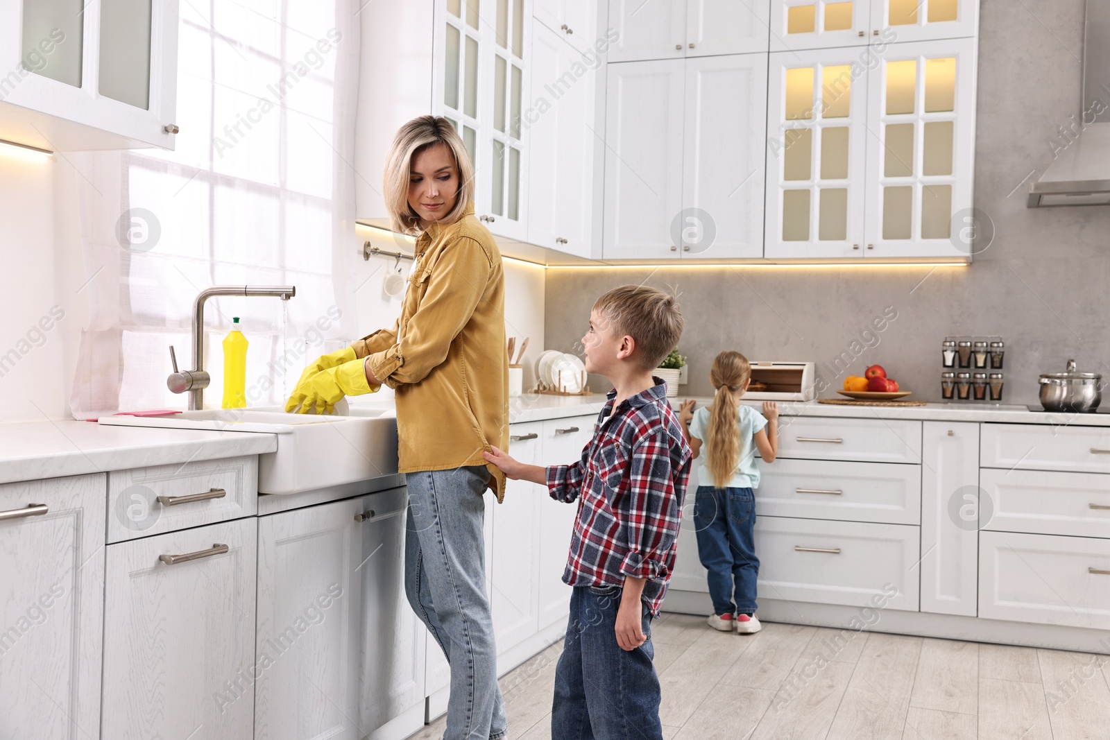 Photo of Housewife washing dishes while her kids playing in kitchen