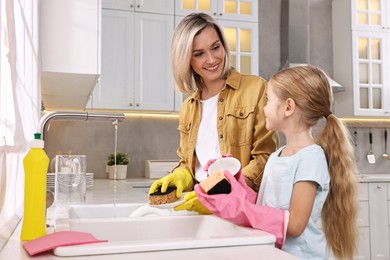 Photo of Happy housewife and her daughter washing dishes in kitchen together