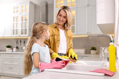 Happy housewife and her daughter washing dishes in kitchen together