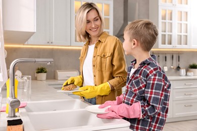 Photo of Happy housewife and her son washing dishes in kitchen together