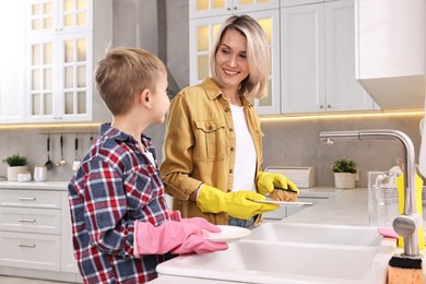 Photo of Happy housewife and her son washing dishes in kitchen together