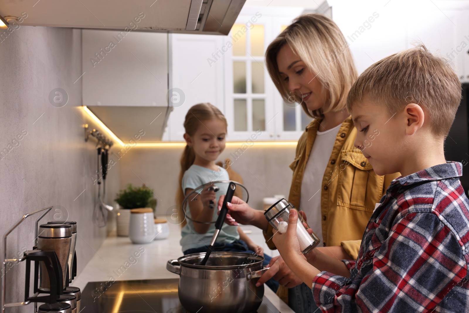 Photo of Happy housewife and her kids cooking together on stove in kitchen