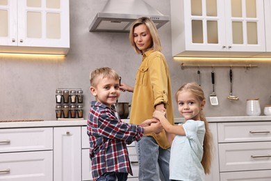 Photo of Housewife cooking on stove while her kids playing and distracting her in kitchen