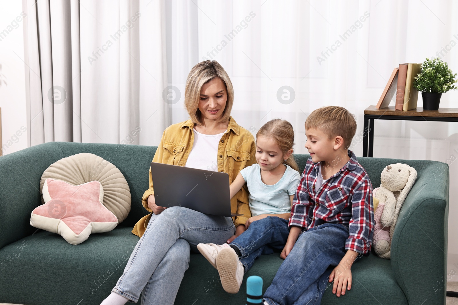 Photo of Housewife spending time with her kids and using laptop on couch at home