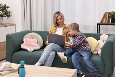 Photo of Housewife spending time with her kids and using laptop on couch at home