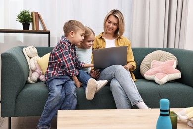 Photo of Housewife spending time with her kids and using laptop on couch at home