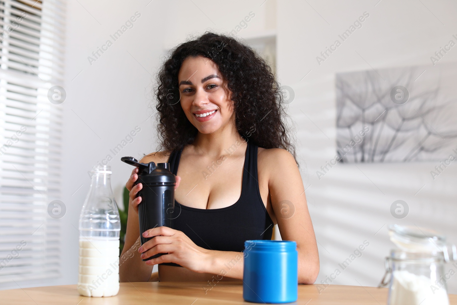 Photo of Beautiful woman making protein shake at wooden table indoors