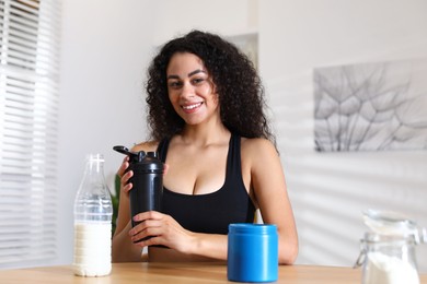 Photo of Beautiful woman making protein shake at wooden table indoors