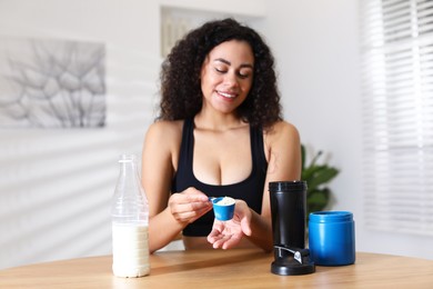 Photo of Beautiful woman making protein shake at wooden table indoors