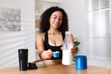 Photo of Beautiful woman making protein shake at wooden table indoors, selective focus