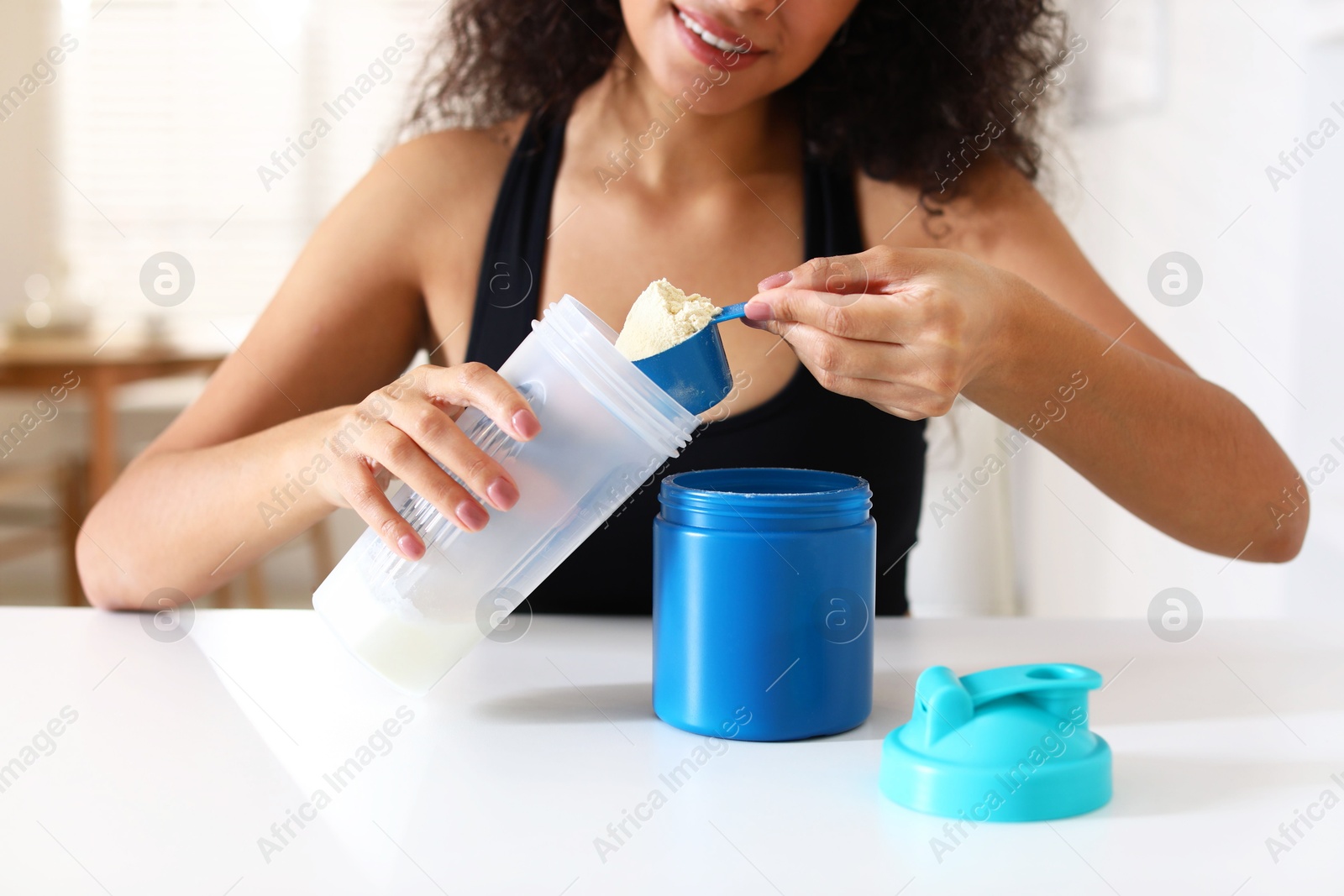 Photo of Beautiful woman making protein shake at white table indoors, closeup