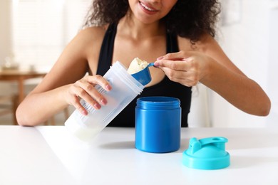 Photo of Beautiful woman making protein shake at white table indoors, closeup