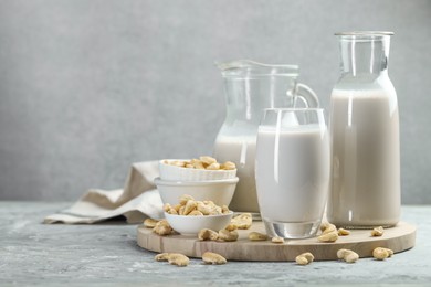 Photo of Glassware with fresh cashew milk and nuts on grey table, space for text