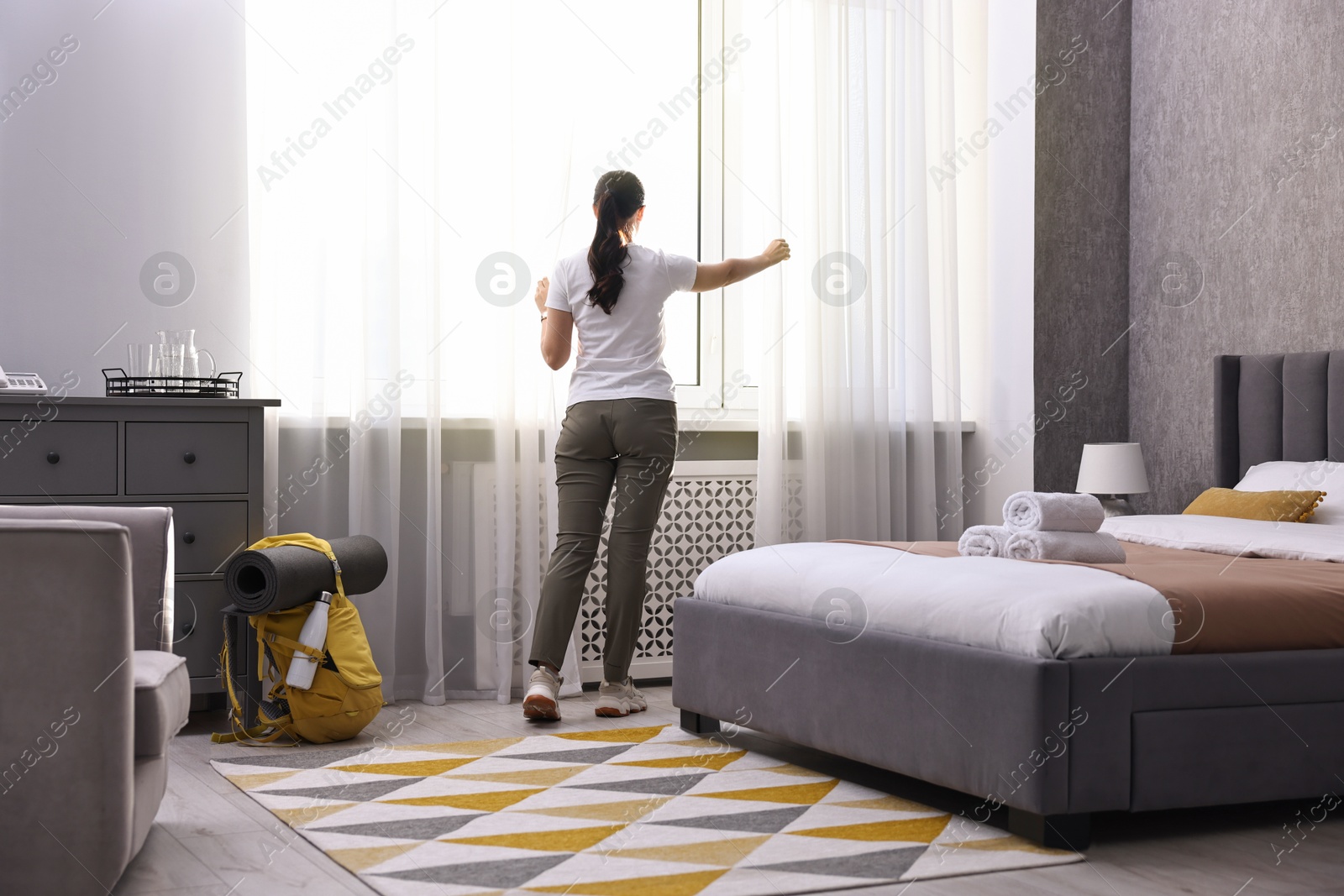 Photo of Traveller opening curtains in hotel room, back view