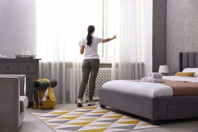 Traveller opening curtains in hotel room, back view