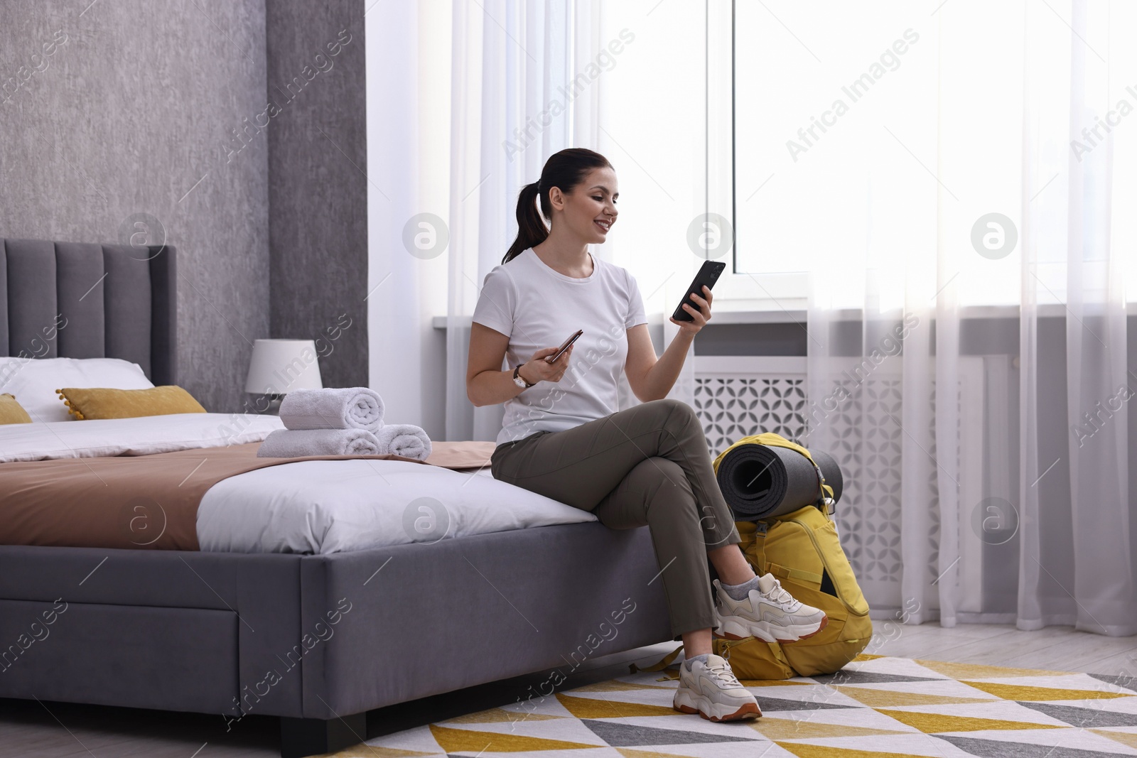 Photo of Traveller with phone, passport and backpack sitting on bed in hotel room