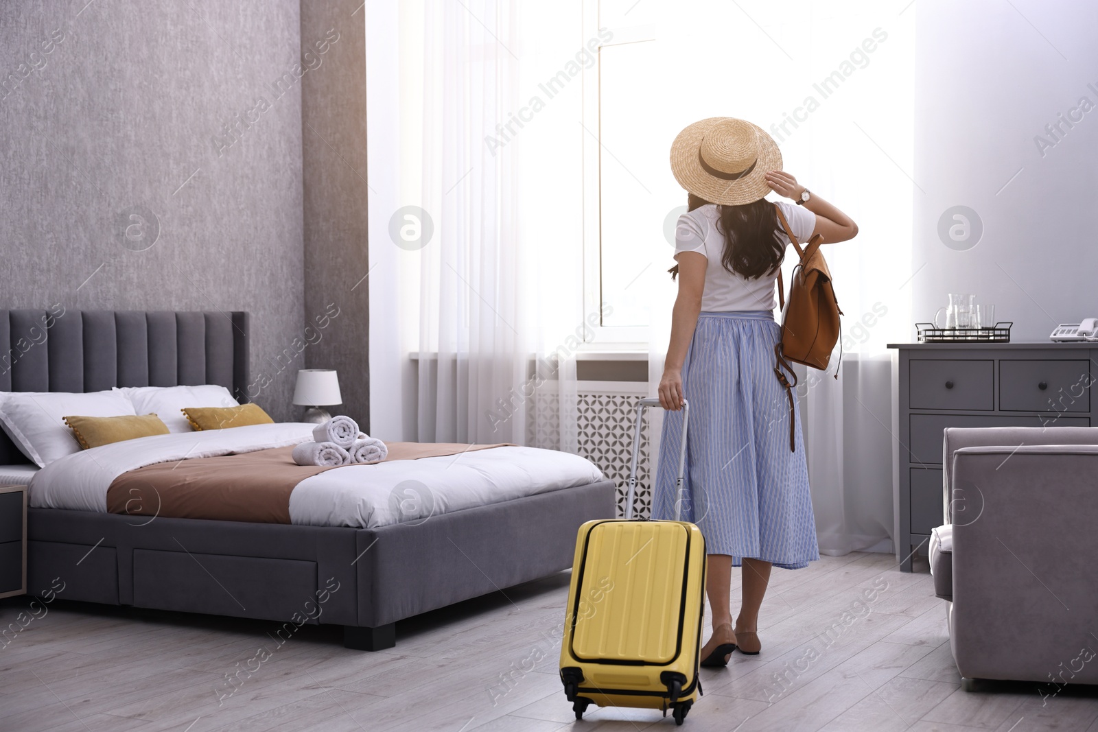 Photo of Traveller with suitcase in hotel room, back view