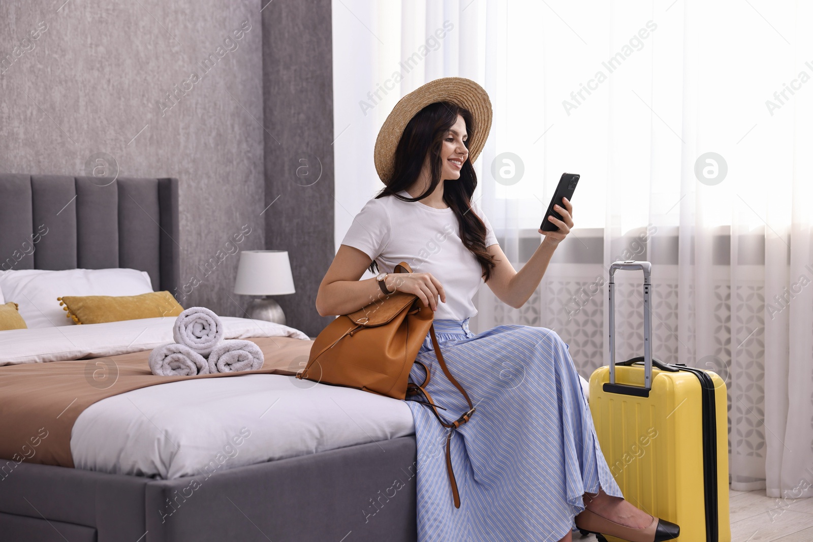 Photo of Traveller with phone and suitcase sitting on bed in hotel room