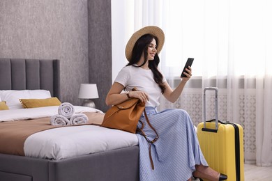 Traveller with phone and suitcase sitting on bed in hotel room