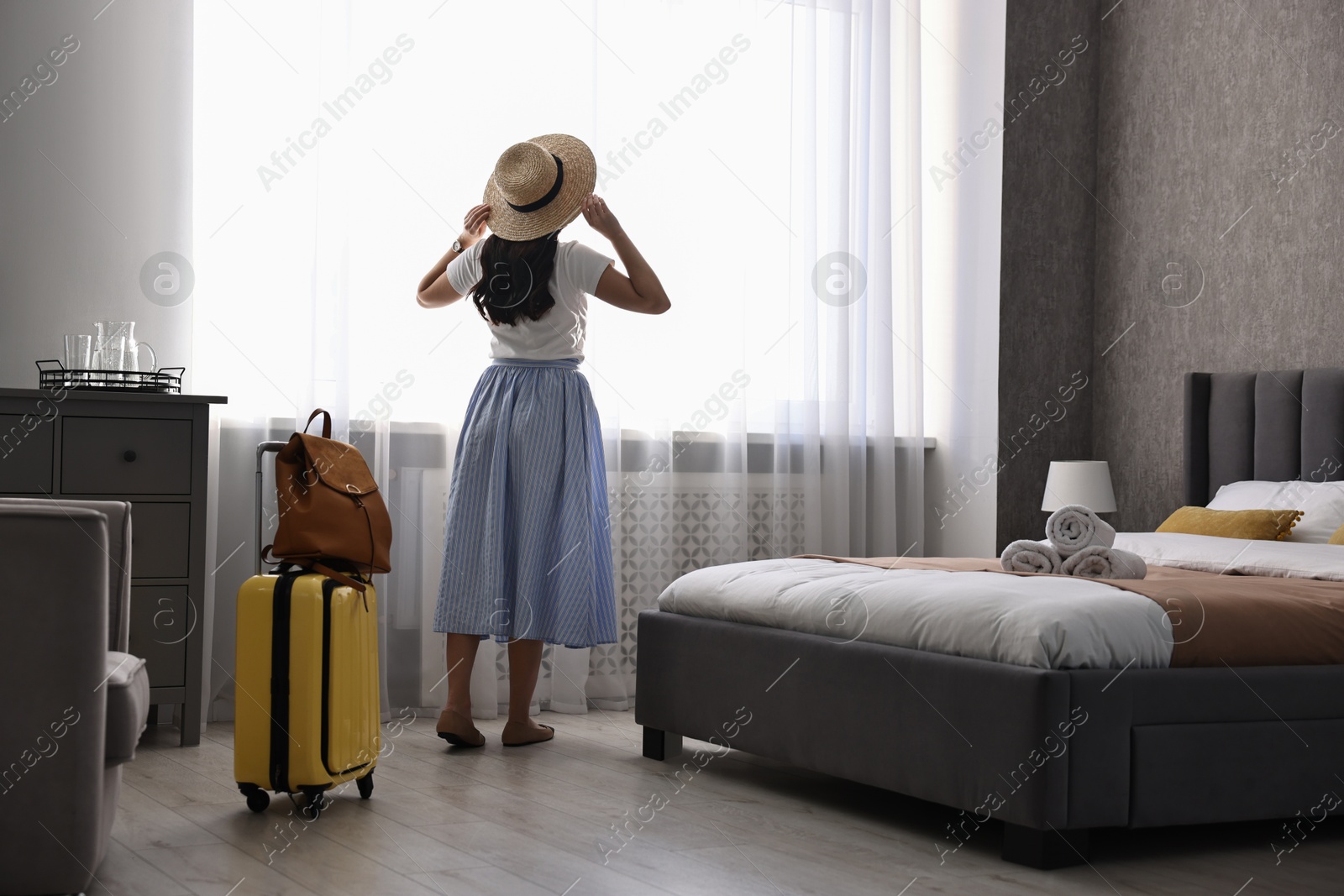 Photo of Traveller with suitcase standing near window in hotel room, back view