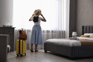 Photo of Traveller with suitcase standing near window in hotel room, back view