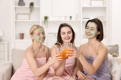 Photo of Spa day. Beautiful women with face masks and healthy drinks on sofa indoors