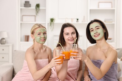 Spa day. Beautiful women with face masks and healthy drinks on sofa indoors