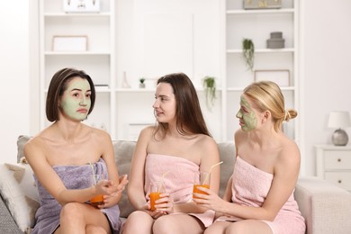 Photo of Spa day. Beautiful women with face masks and healthy drinks on sofa indoors