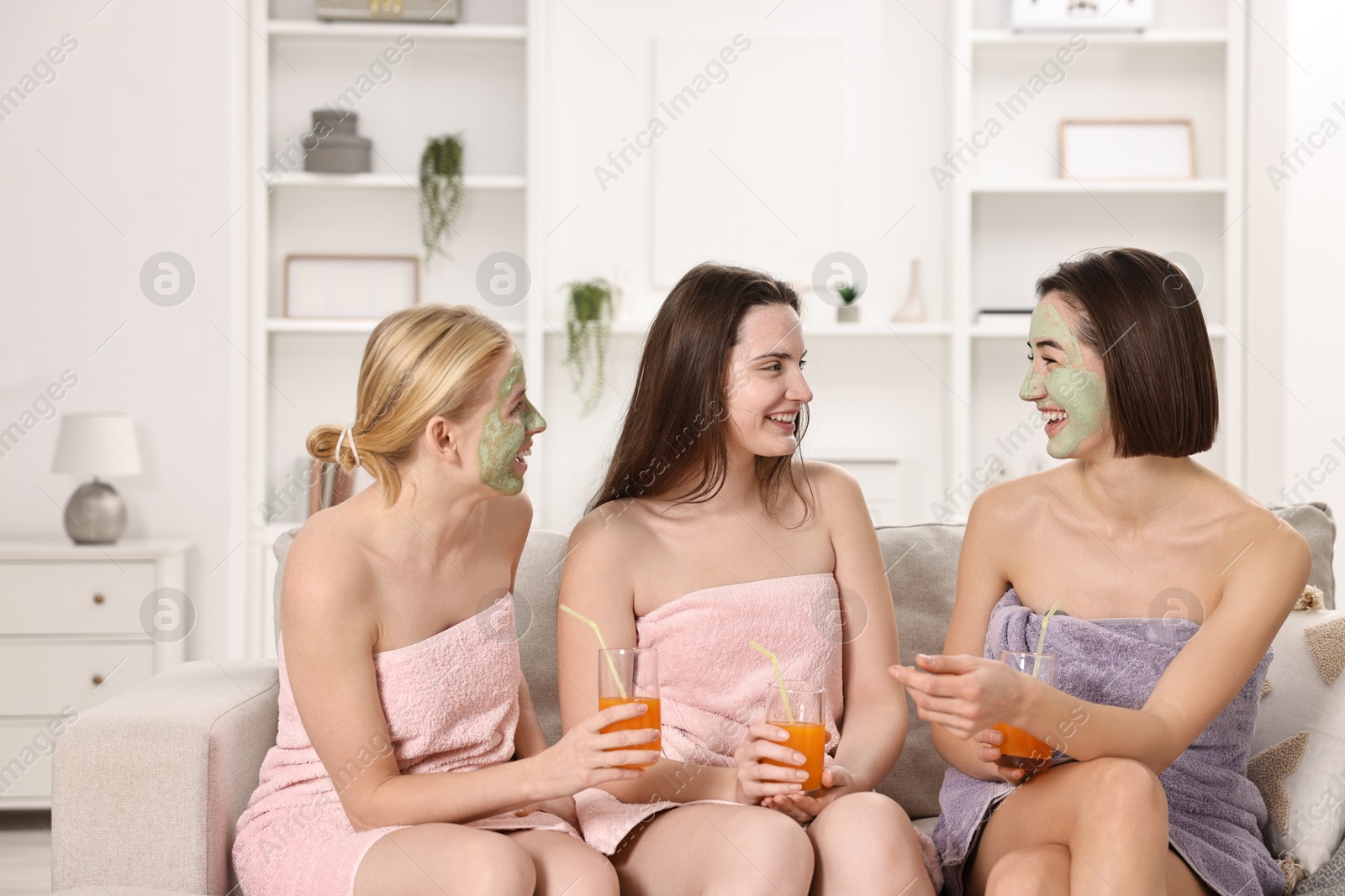 Photo of Spa day. Beautiful women with face masks and healthy drinks on sofa indoors