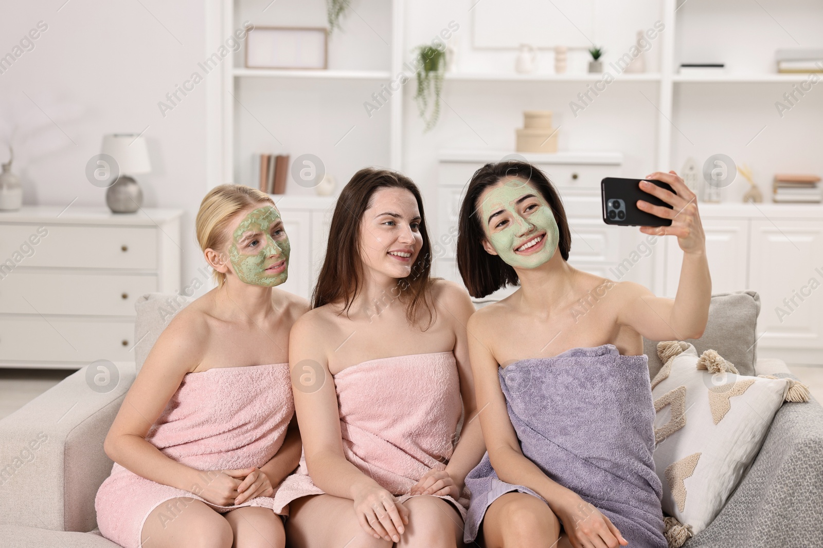 Photo of Spa day. Beautiful women with face masks taking selfie on sofa indoors