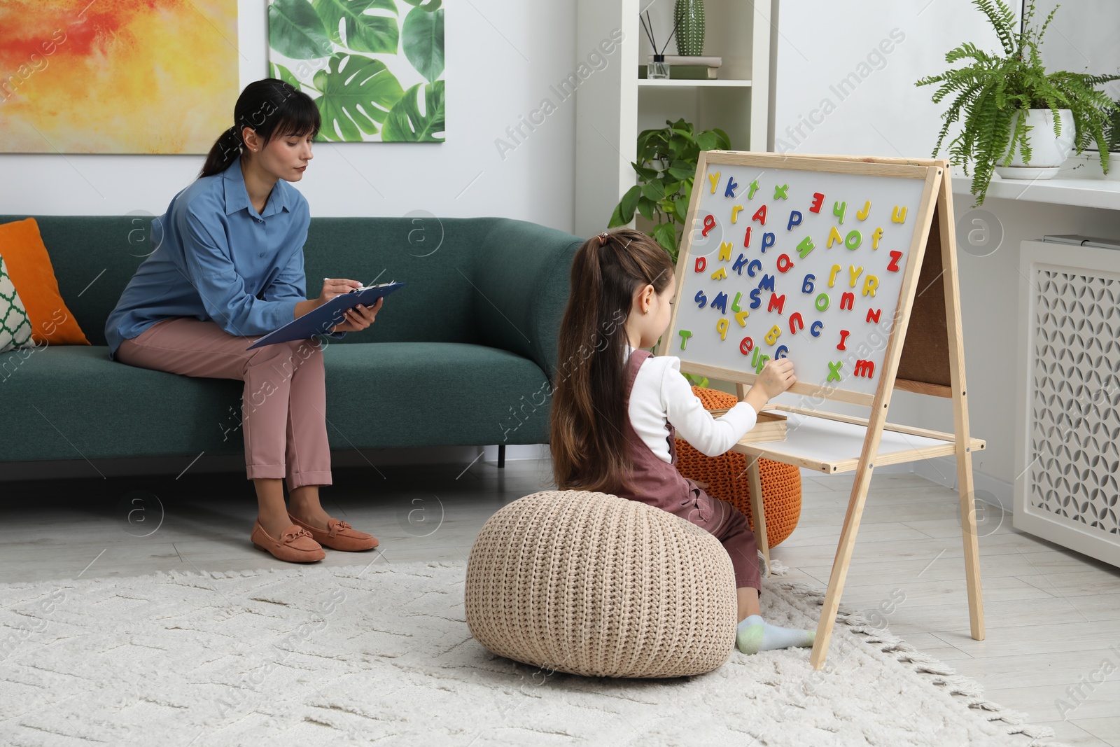 Photo of Girl assembling letters on magnetic board while psychologist taking notes indoors