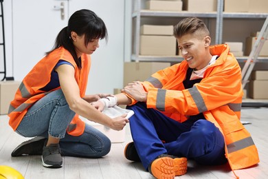 Accident at work. Woman putting bandage on her colleague's injured wrist in warehouse