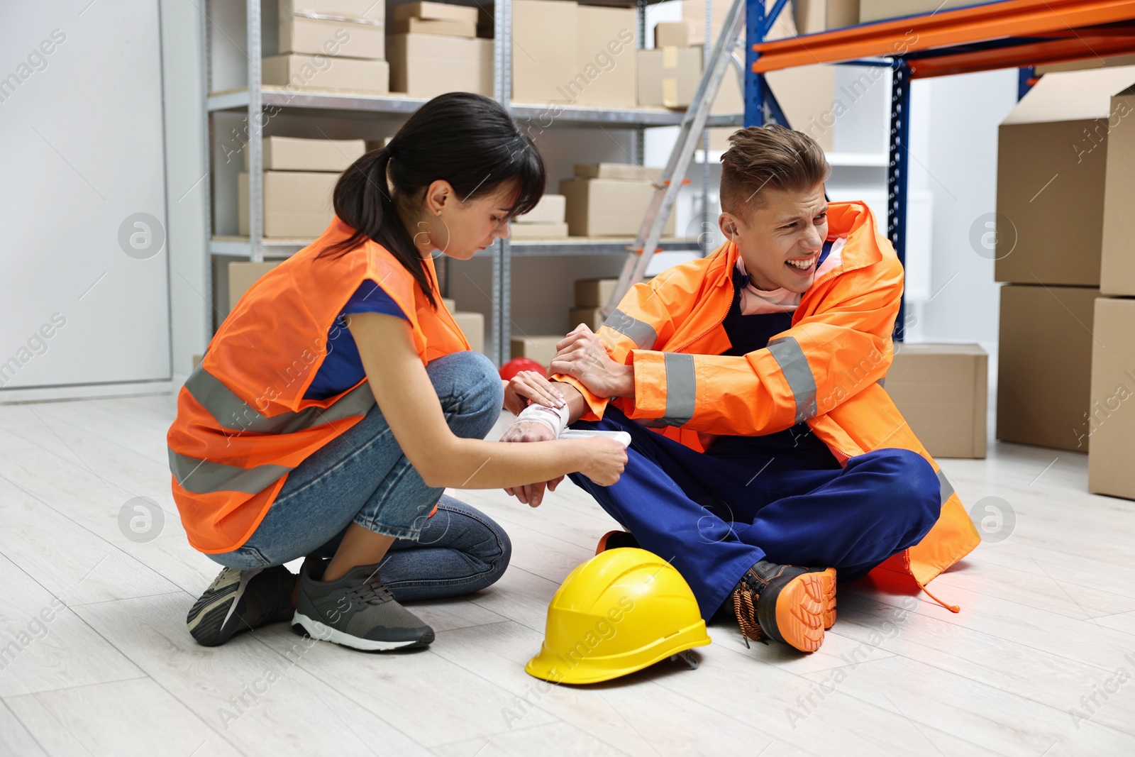 Photo of Accident at work. Woman putting bandage on her colleague's injured wrist in warehouse