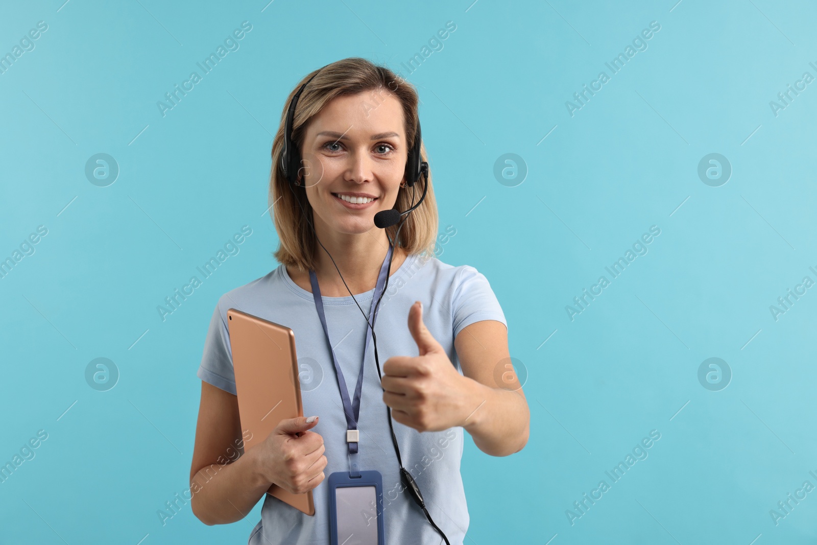 Photo of Technical support call center. Smiling operator with tablet showing thumbs up on light blue background, space for text