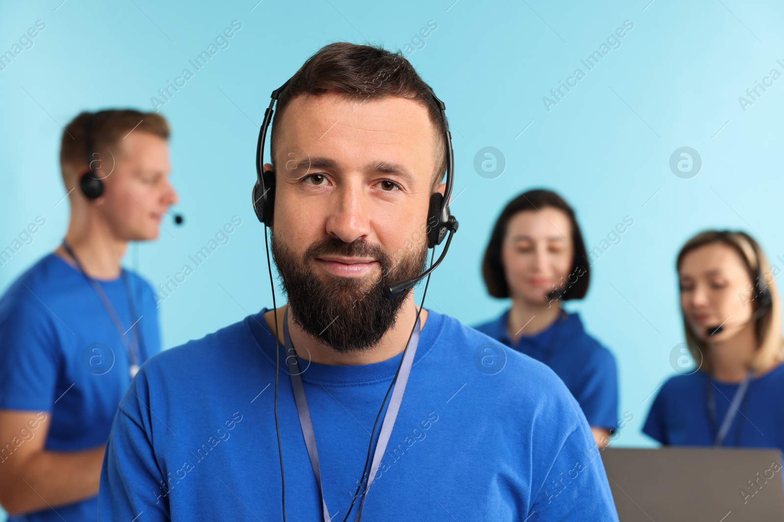 Photo of Technical support call center. Team of friendly operators working on light blue background