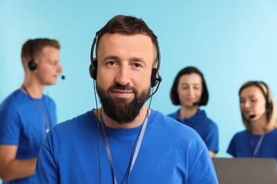 Photo of Technical support call center. Team of friendly operators working on light blue background