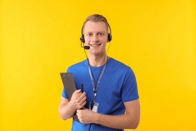 Photo of Technical support call center. Smiling operator with clipboard on yellow background