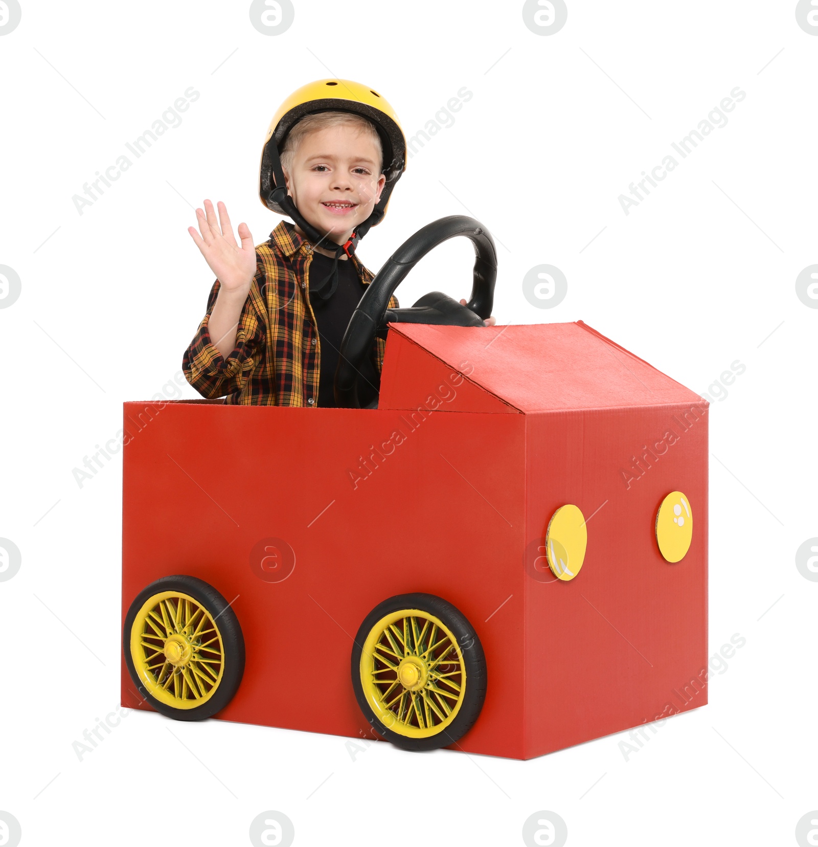 Photo of Little boy waving while driving car made of cardboard on white background