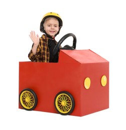 Little boy waving while driving car made of cardboard on white background