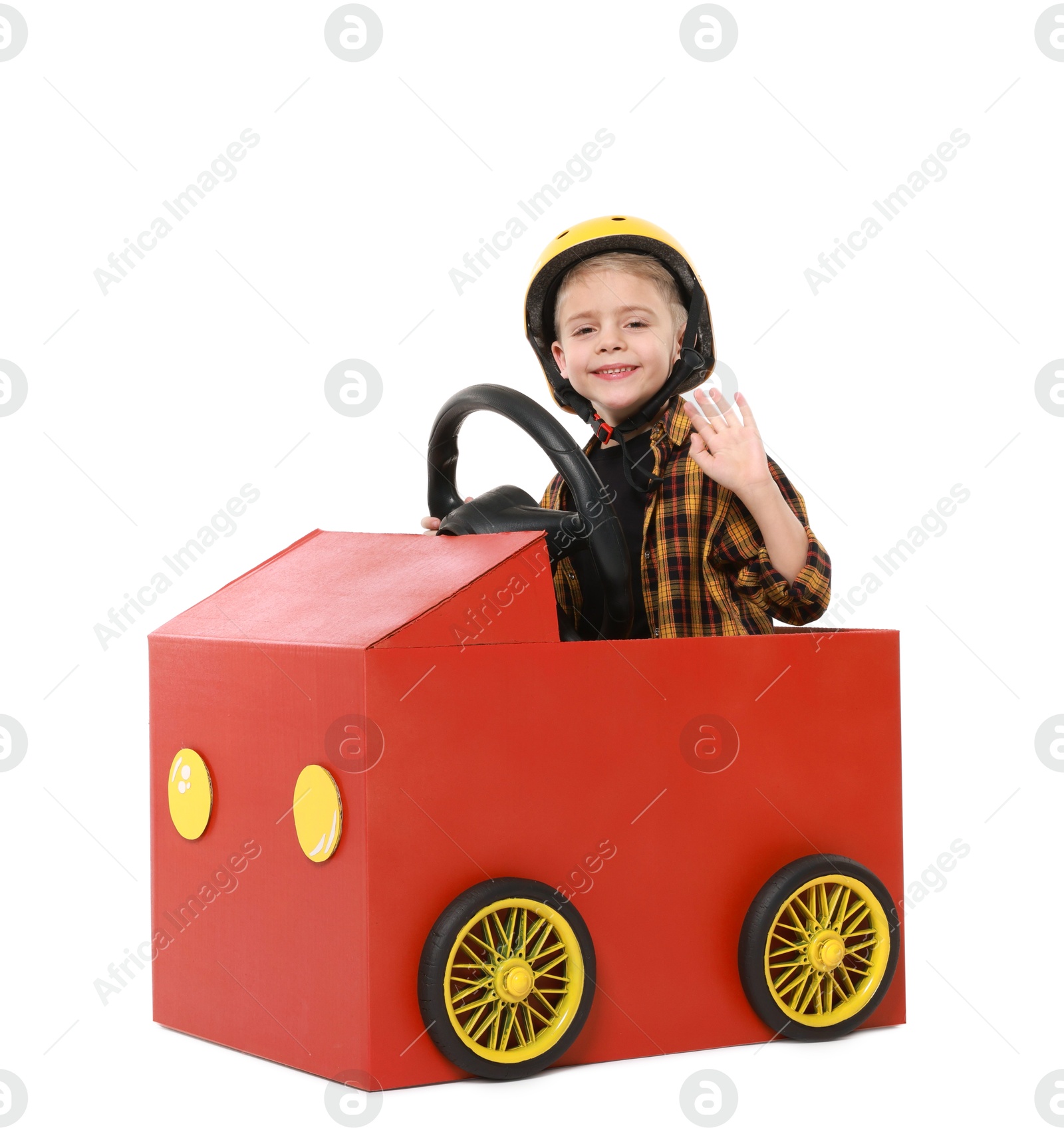 Photo of Little boy waving while driving car made of cardboard on white background