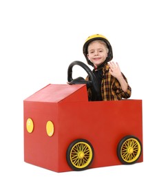 Photo of Little boy waving while driving car made of cardboard on white background