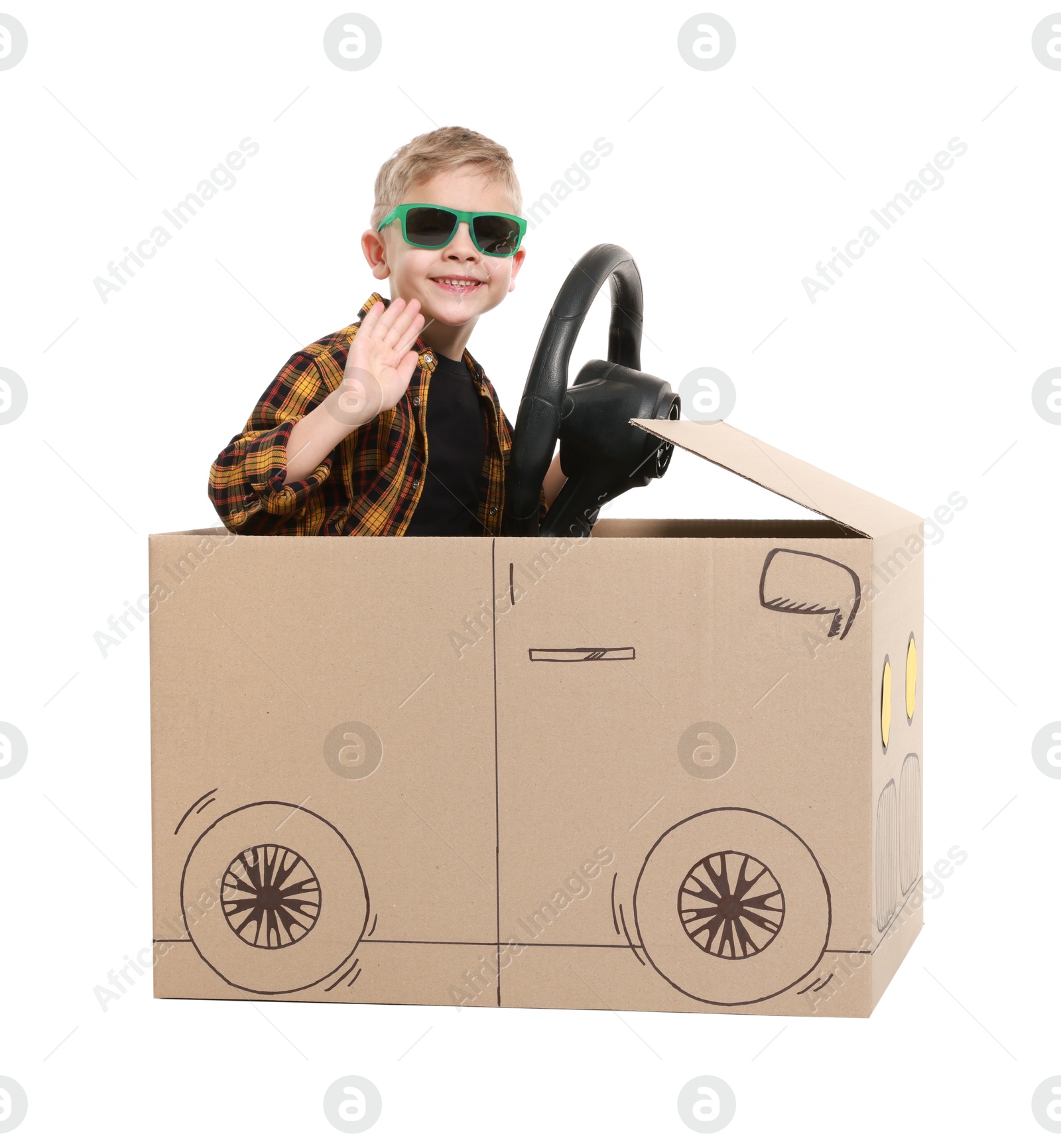 Photo of Little boy waving while driving car made of cardboard on white background