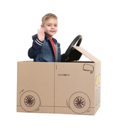 Little boy waving while driving car made of cardboard on white background