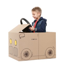 Little boy driving car made of cardboard on white background