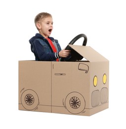 Little boy driving car made of cardboard on white background